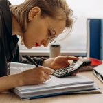 Profissional analisa documentos contábeis ao lado de uma calculadora em um ambiente de trabalho.