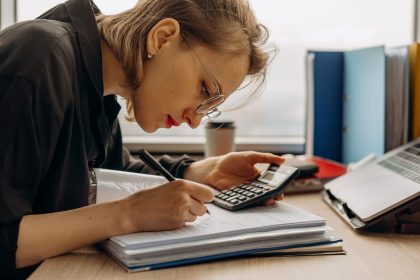 Profissional analisa documentos contábeis ao lado de uma calculadora em um ambiente de trabalho.