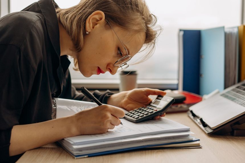 Profissional analisa documentos contábeis ao lado de uma calculadora em um ambiente de trabalho.