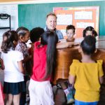 Professor orienta crianças durante uma aula de música ao redor de um piano.