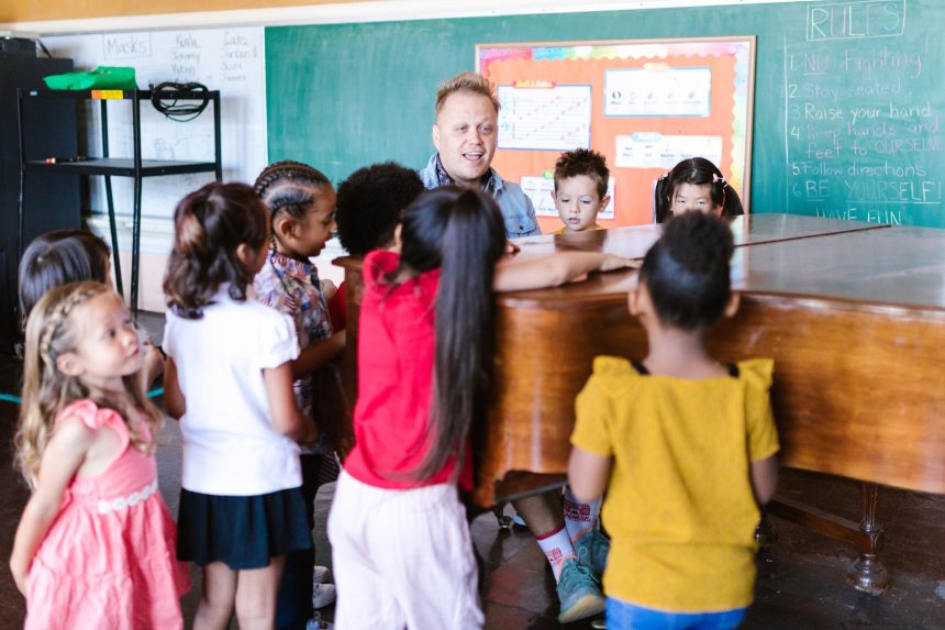 Professor orienta crianças durante uma aula de música ao redor de um piano.