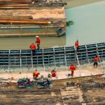Vista aérea de trabalhadores e máquinas construindo uma estrutura de canalização junto a um curso d’água.