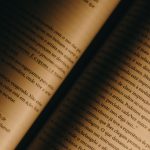 Close de páginas amareladas de um livro aberto, com texto em português e iluminação quente.