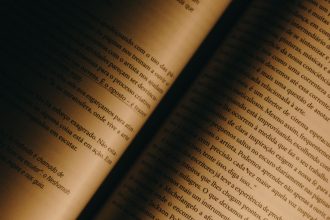 Close de páginas amareladas de um livro aberto, com texto em português e iluminação quente.