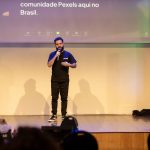 Homem fala ao microfone em um palco durante uma apresentação pública