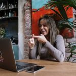 Mulher faz sinais em Libras durante uma videochamada em um laptop, em ambiente interno.
