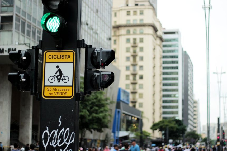 Semáforo e placa de travessia para bicicletas em uma rua movimentada de São Paulo.