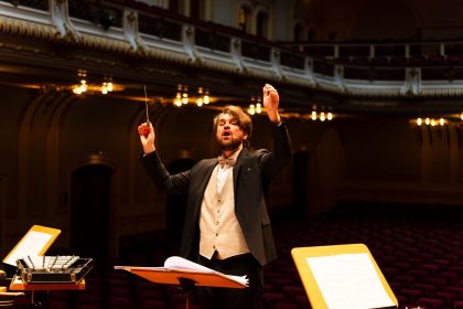 Maestro rege uma orquestra durante apresentação em uma elegante sala de concertos.