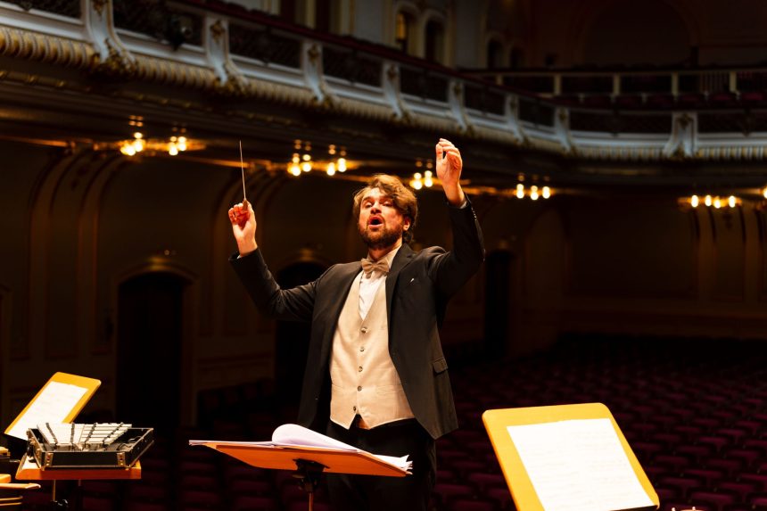 Maestro rege uma orquestra durante apresentação em uma elegante sala de concertos.